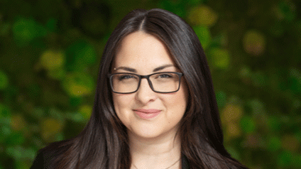 Smiling person with glasses in front of blurred green foliage.