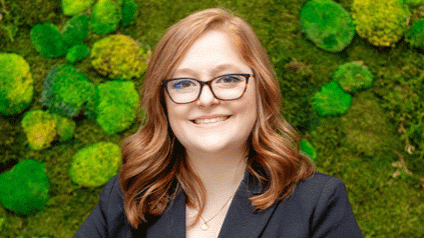 Marissa smiling and facing camera; green moss wall in background.