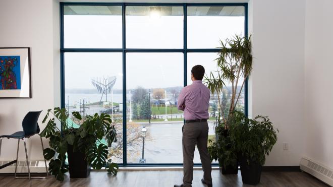 Person standing in front of window with arms crossed. The subject is looking out through the window.