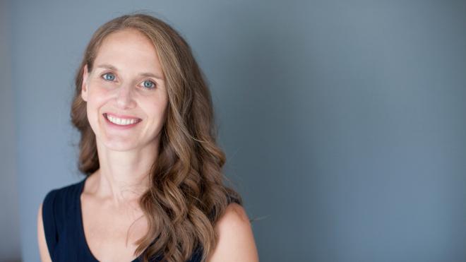 Lindsay Zier-Vogel Headshot - long haired woman smiling in front of dusty blue background
