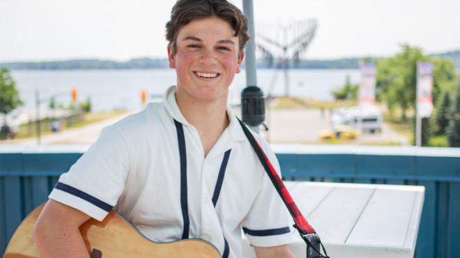 Young man holding a guitar with the Spirit Catcher in the background