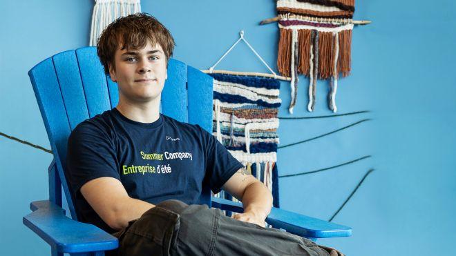 Young man sitting on a blue chair against a blue wall with woven art.