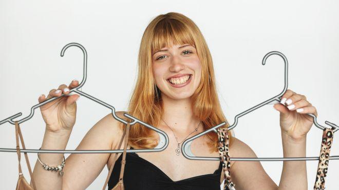 Smiling woman holding two hangers with clothing.