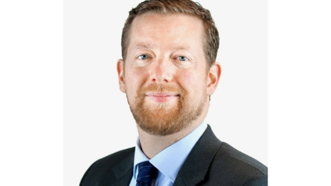 Portrait of a bearded man in a suit and tie, smiling slightly.