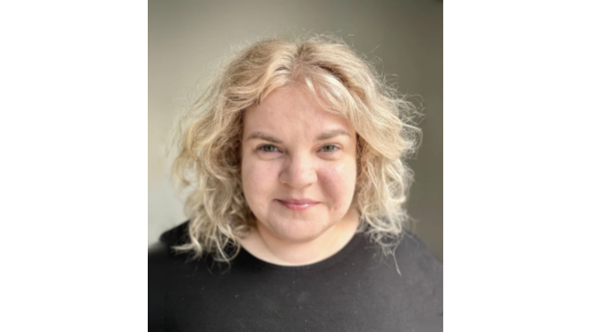 Smiling person with curly blonde hair wearing a black shirt.