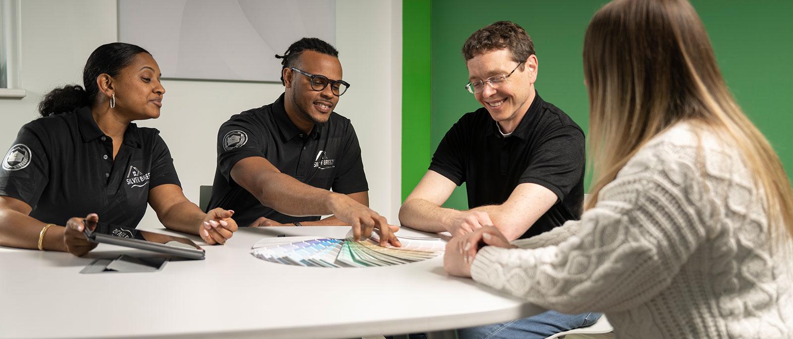 Group discussing paint swatches around a table, three wearing branded polo shirts.
