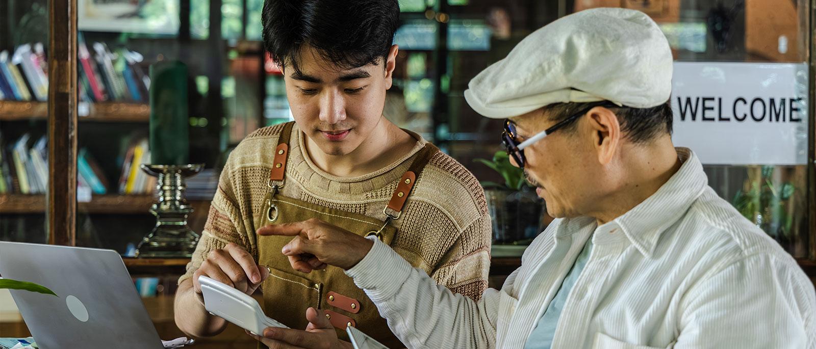 Man and older gentleman discussing something on a tablet in a business.