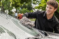 Young person smiling while washing a car windshield outdoors.
