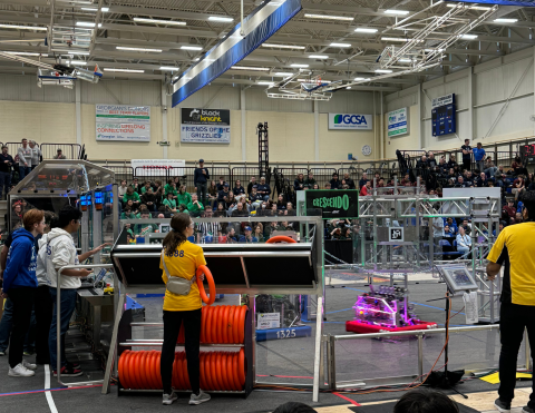 Robotics competition in a gymnasium with spectators and referees.