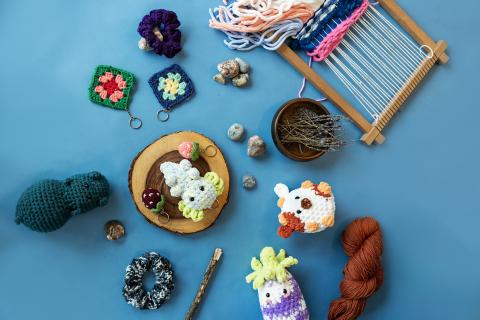 Crochet yarn crafts on blue surface with a loom, balls of yarn, and small decorations.
