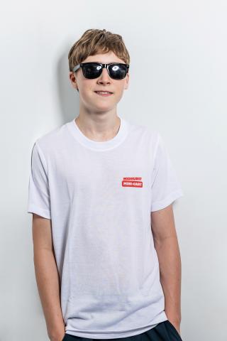Teenager in sunglasses and white t-shirt, leaning against a white wall, smiling.