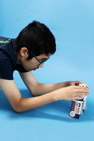 Boy in glasses builds with toy blocks on a blue background.