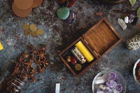 Wooden box with stones and a candle, surrounded by various herbs and crystals.