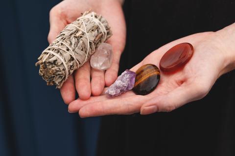 Hands holding sage bundle, crystals, and stones.