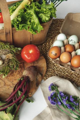 Fresh vegetables, eggs, and flowers on a woven mat.