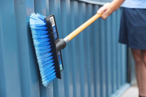 Person cleaning a blue fence with a blue-bristled brush.