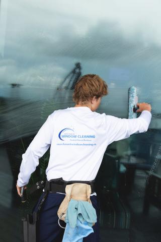 Worker cleaning a large window with a squeegee.
