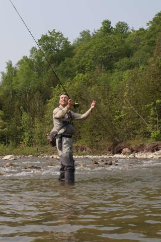 Person fly-fishing in a river surrounded by trees.