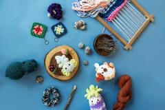 Crochet yarn crafts on blue surface with a loom, balls of yarn, and small decorations.