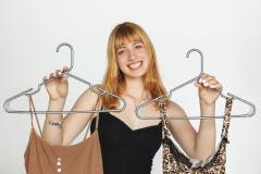 Smiling person holds two dresses on hangers against a white background.