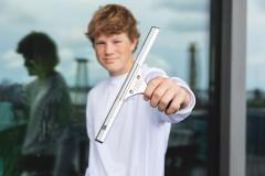 Teen holding a window squeegee, standing next to a reflective glass surface.