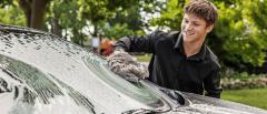 Young person smiling while washing a car windshield outdoors.