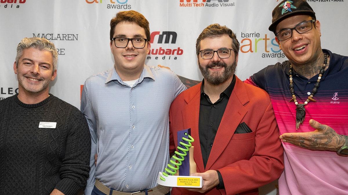 Four people standing in front of a backdrop with logos for Barrie Arts Awards, MacLaren Art Centre, Rhubarb Media, Allegra Barrie and MTAV. One of the people is holding an award.